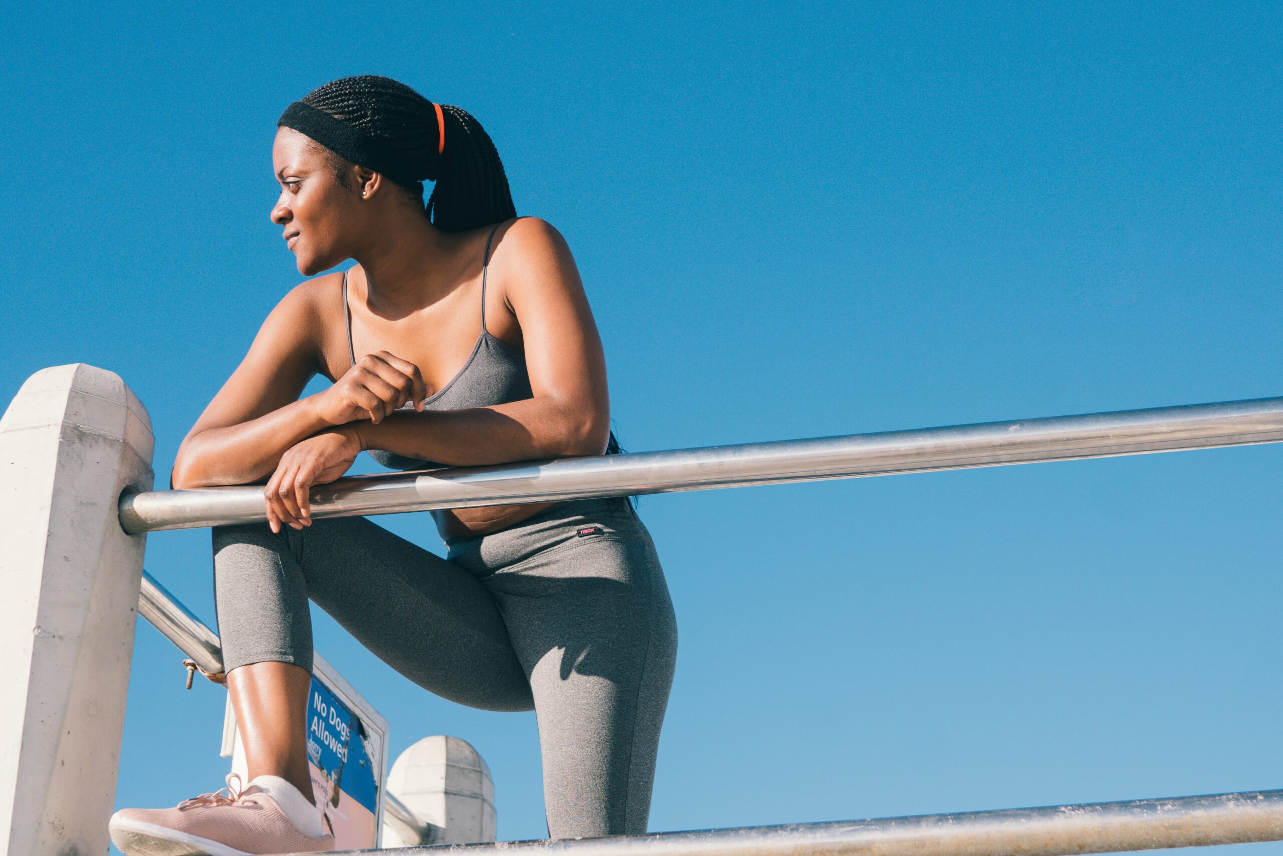 Image of a woman in gym clothing, leaning on a fence as though she has just been for a run